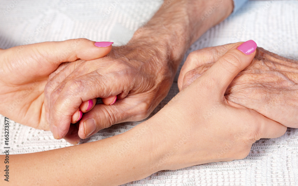 Old and young holding hands on light background, closeup. Care is at home of elderly
