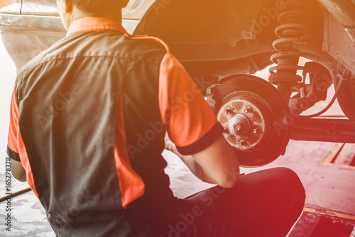 Professional car mechanic changing wheel in auto repair service. worker repairs brake pads in garage station