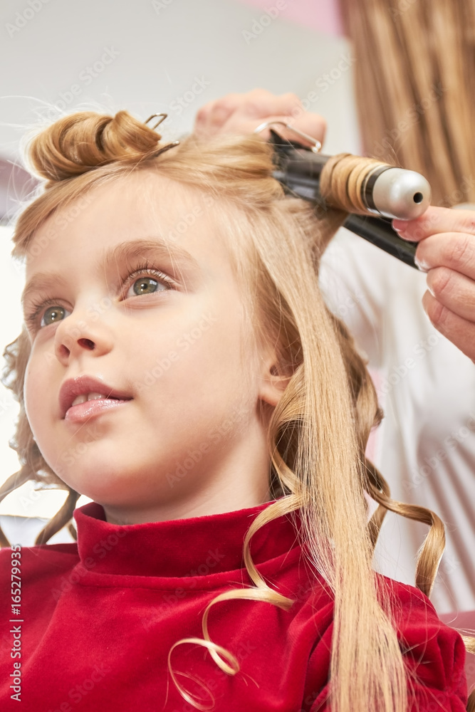 Fototapeta premium Little girl and curling iron. Child at hairdresser close up.