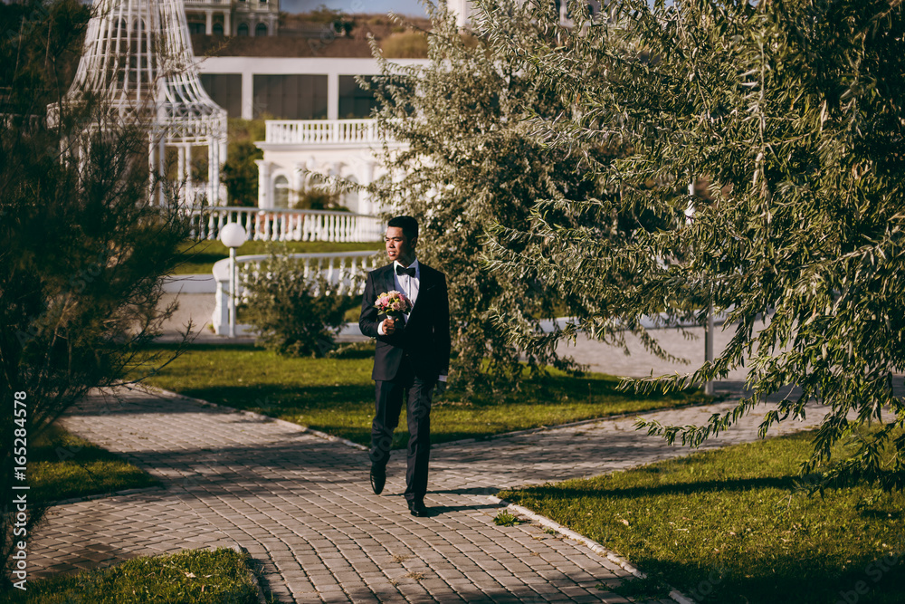 Groom with bouquet on a promenade on the waterfront