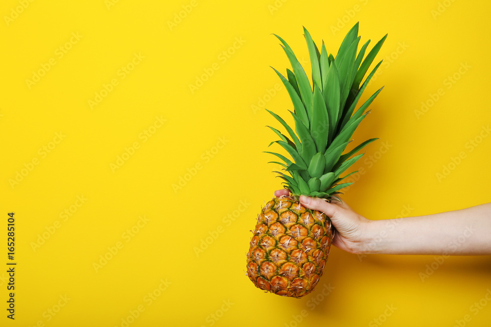 Female hand holding ripe pineapple on yellow background Female hand holding ripe pineapple on yellow background