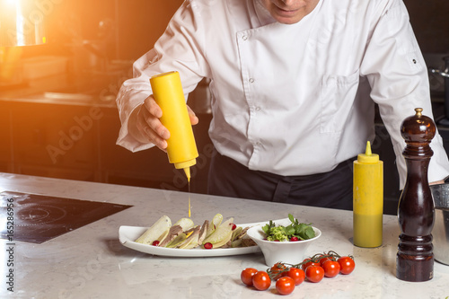 Chef plating up food in a restaurant pouring a gravy or sauce over the meat before serving it to the customer, close up view of his hand and the gravy boat photo