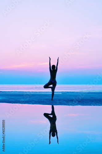 Silhouette woman practicing yoga on the beach at sunset.