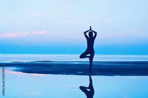 Silhouette woman practicing yoga on the beach at sunset.