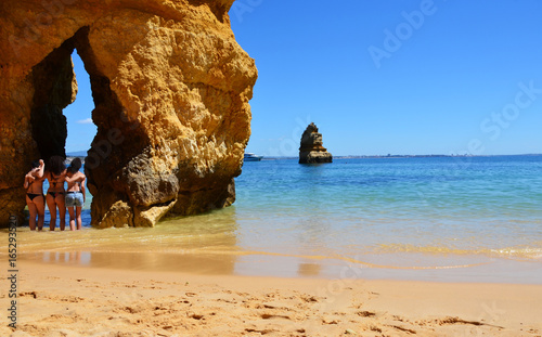 Girls posing at famous gap between rocks at Camilo Beach (Praia do Camilo) at Algarve, Portugal with turquoise sea in background