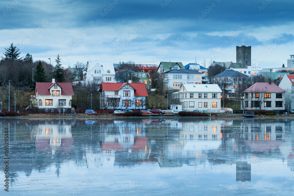 Beautiful reflection of the cityscape of Reykjavik in lake Tjornin at the blue hour in winter with the Basilica of Christ the King (Landakotskirkja)