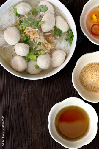 White noodle with pork ball soup in white bowl with seasoning on brown wooden floor thai food / Still Life food, selective focus and space for text