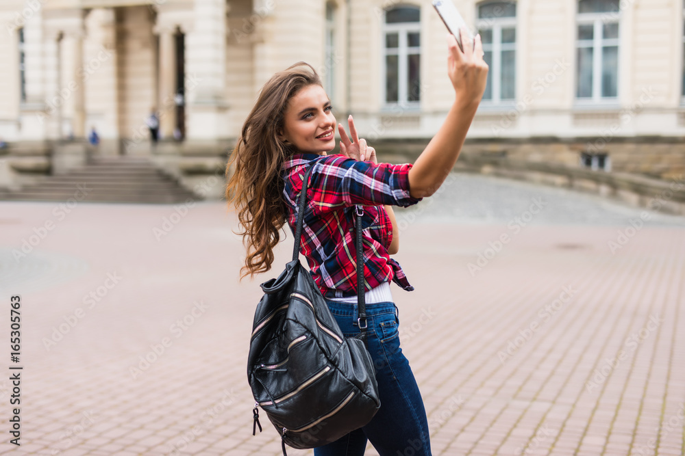 Young attractive playful tourist is making selfie on the phone outside wearing hat sunglasses