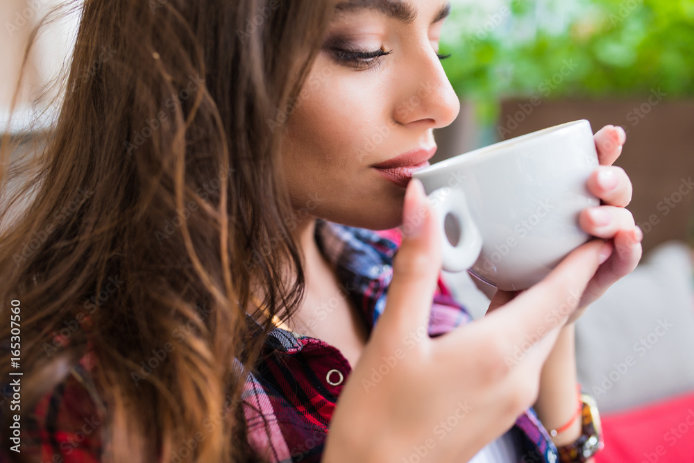 Charming woman in a cafe drinking coffee in street cafe. Summer