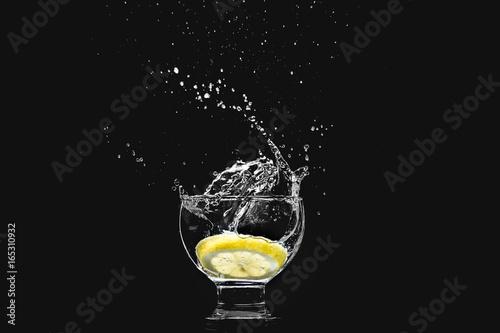 Splash in a glass of pure water with a lemon isolated on a black background