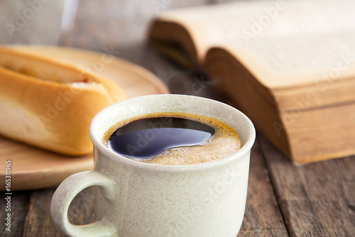 Close up view of coffee cup with bread and books on old wood flo