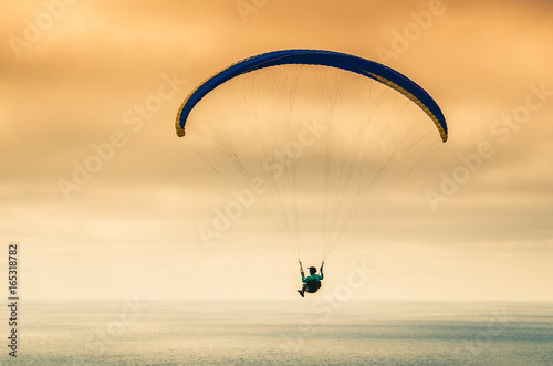 Hang glider flying over the ocean against the sunset sky 