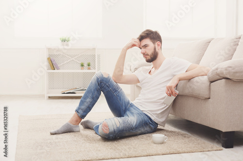 Pensive young man at home with mobile