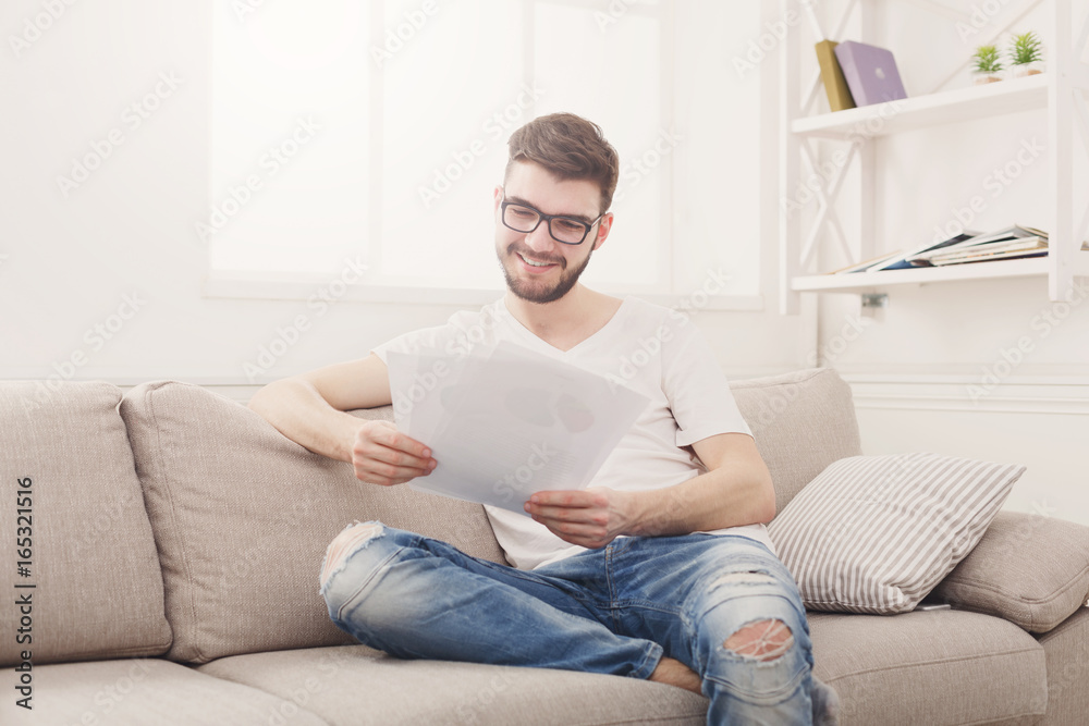Happy young businessman reading paperwork at home
