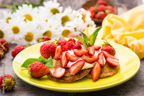 Fritters with yogurt, sliced strawberries and mint leaves on a plate and a bouquet of daisies