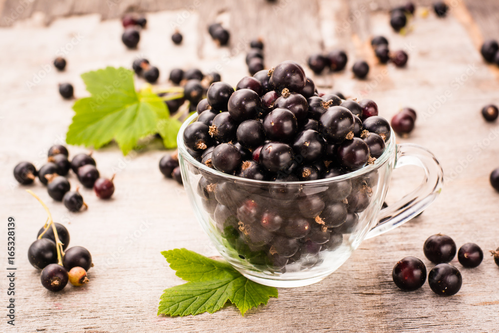 Fresh black currant in the cup and leaves on a wooden table Fresh black currant in the cup and leaves on a wooden table