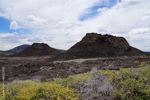 Two spatter cones and one cinder cone rising above a landscape of black volcanic basalt rock from eruptions along the Great Volcanic Rift Zone, a line of cones and lava vents. Craters of the Moon, USA
