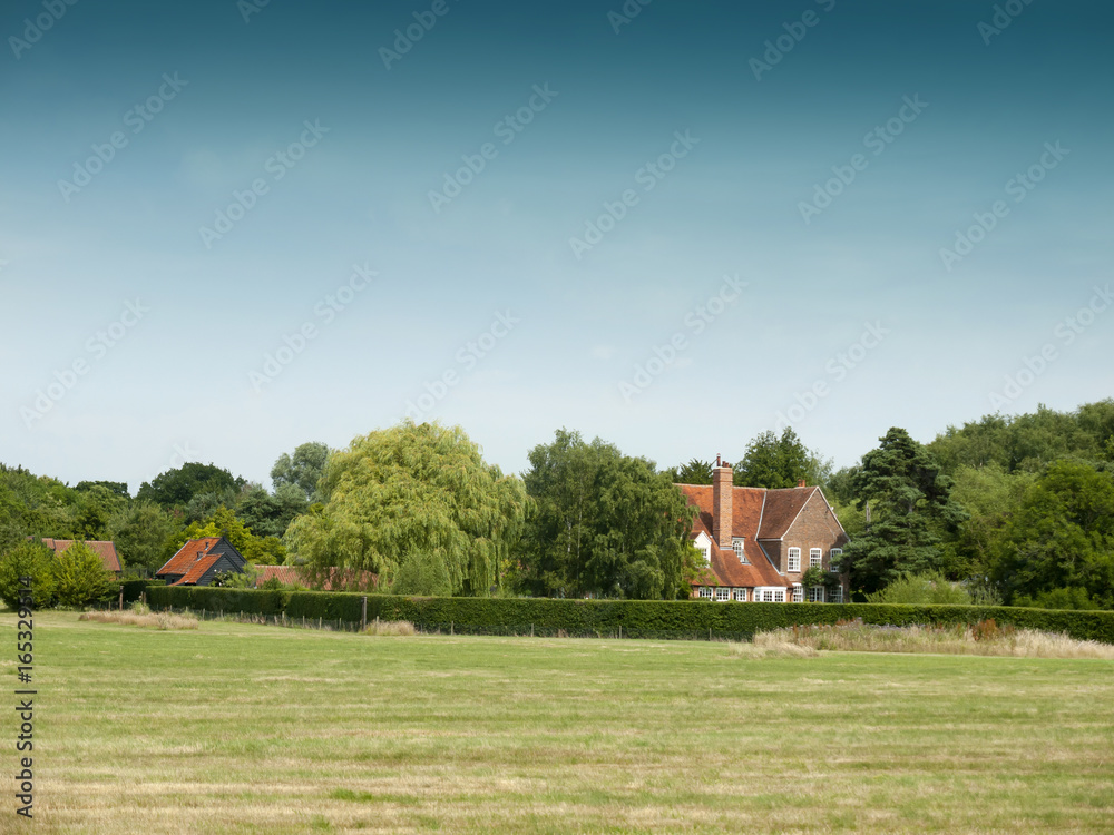 Obraz premium country farm house behind trees and field