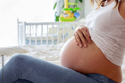 Free Download Happy young beautiful pregnant woman, sitting on bed in bedroom - GFXLoad