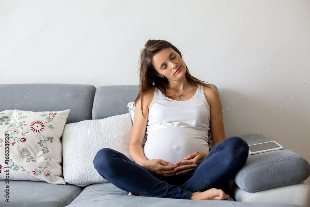 Young pregnant woman, sitting on couch in living room Young pregnant woman, sitting on couch in living room