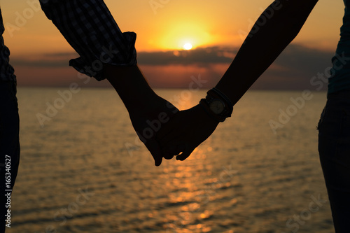 A loving couple (silhouettes of a man and a girl) hold hands in the rays of light at sunset on the sea on a pier. photo