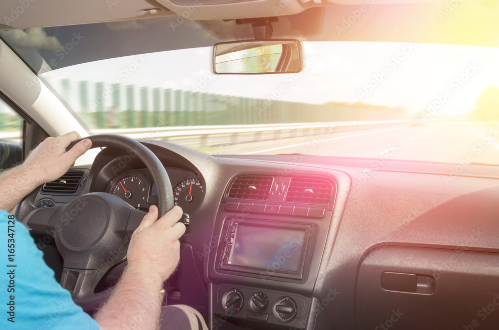 A person is driving a car, at speed along the route to the sunset. Listens to music, uses built-in stereo with navigation. Travel. A man holding a mobile phone with a GPS application in the car.