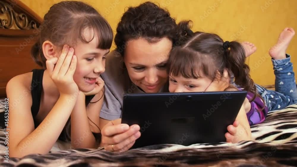 A happy mother with her daughters is looking at the tablet. Laughter mom with her daughters. A happy mother with her daughters is looking at the tablet. Laughter mom with her daughters.