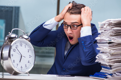 Businessman with pile stack of paper paperwork and an alarm cloc photo