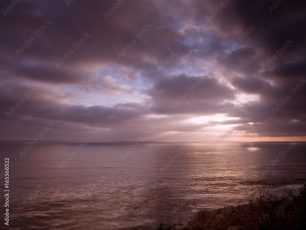 Beams of sunlight show through a cloudy sky onto the ocean