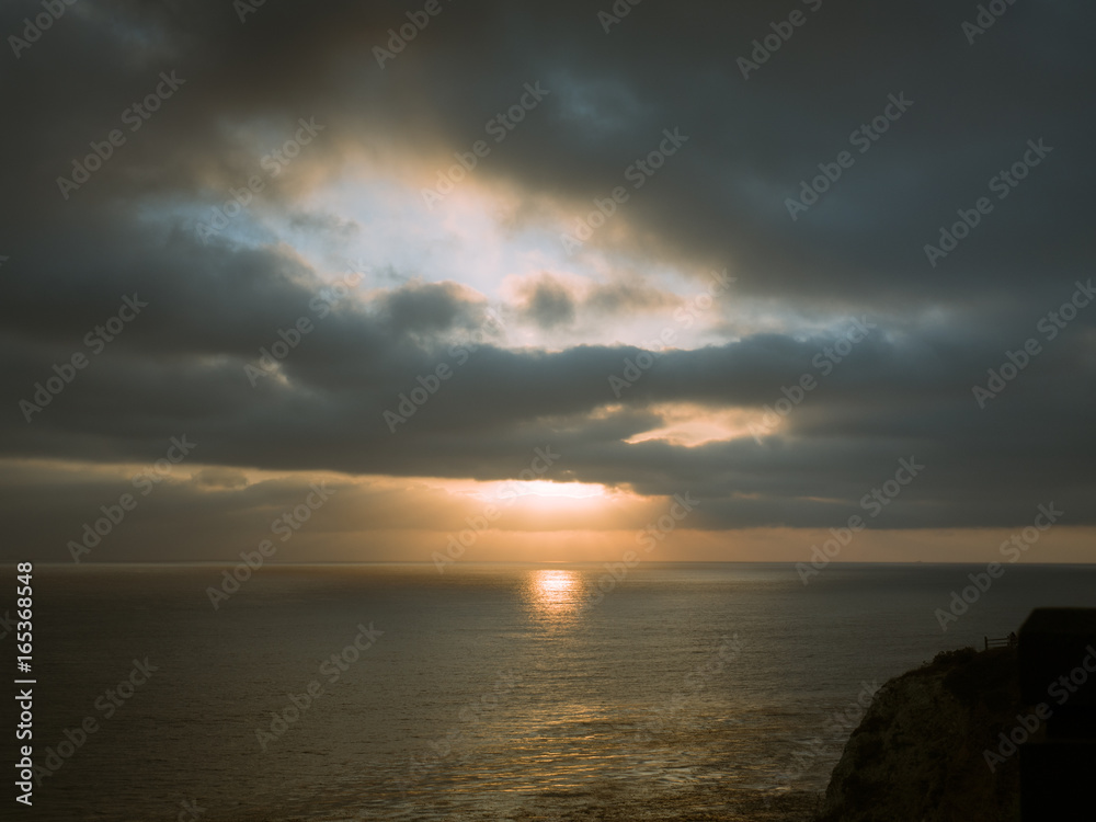 Obraz premium Beams of sunlight show through a cloudy sky onto the ocean