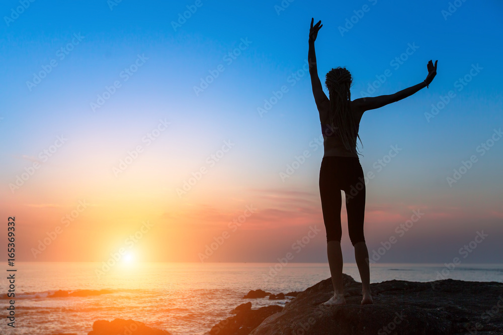 Silhouette of dancing young slim woman on the ocean coast during an amazing sunset.