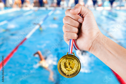 Photography handful of asian man holding gold medal with blurry background of swimming pool