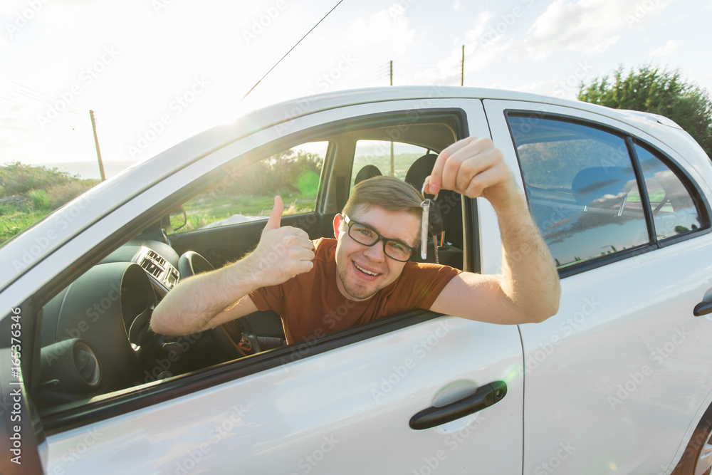 Naklejka premium Young man smiling and holding key in his car. Auto purchase and people concept