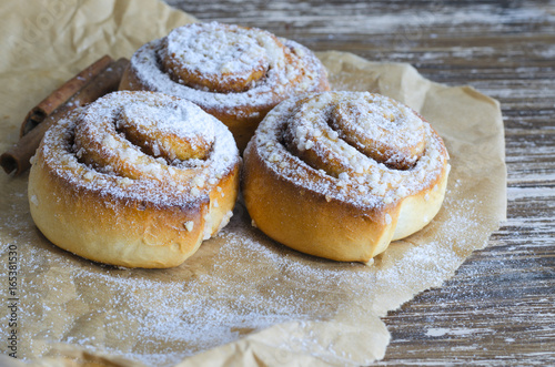 Fresh Delicious  cinnamon  rolls with powdered sugar, metal strainer and cinnamon stick on wooden table. Sweet food background. photo