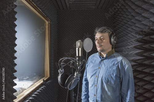 Musician standing by microphone with headphones in recording studio photo