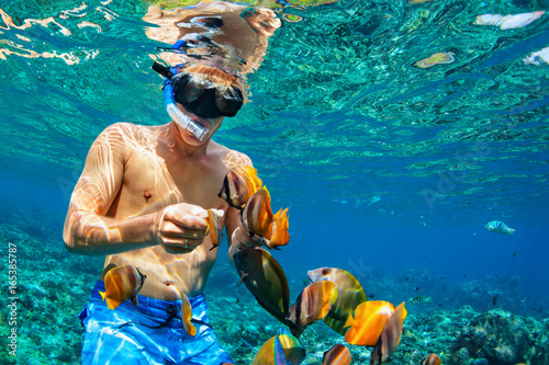 Canvas Print Happy family vacation - man in snorkeling mask dive underwater with tropical fishes in coral reef sea pool