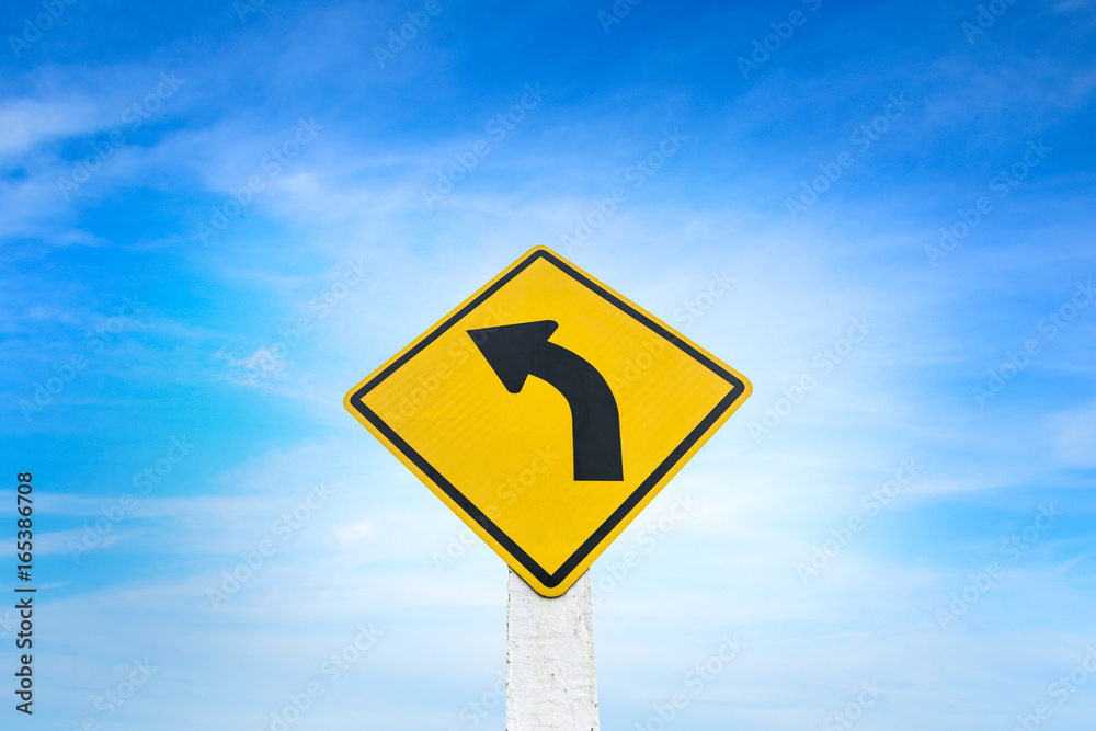 Yellow road sign indicating left turn with blue sky background. Yellow road sign indicating left turn with blue sky background.