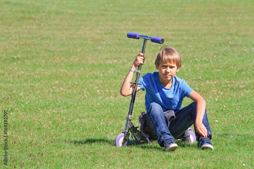 Fototapeta premium Boy sitting on a scooter in the park