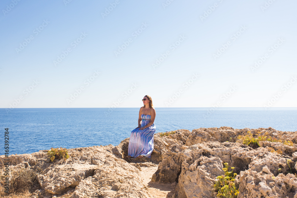 Beautiful woman in a striped dress sitting on the beach. Relaxed woman breathing fresh air,emotional sensual woman near the sea, enjoying summer. Travel and vacation. Freedom and inspiration concept