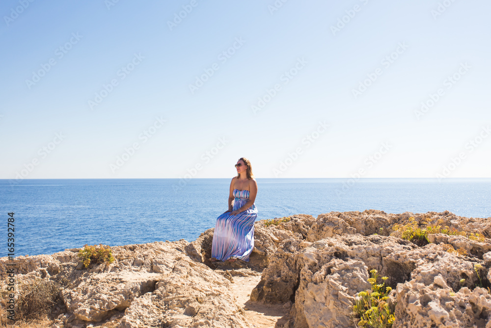 Beautiful woman in a striped dress sitting on the beach. Relaxed woman breathing fresh air,emotional sensual woman near the sea, enjoying summer. Travel and vacation. Freedom and inspiration concept Beautiful woman in a striped dress sitting on the beach. Relaxed woman breathing fresh air,emotional sensual woman near the sea, enjoying summer. Travel and vacation. Freedom and inspiration concept