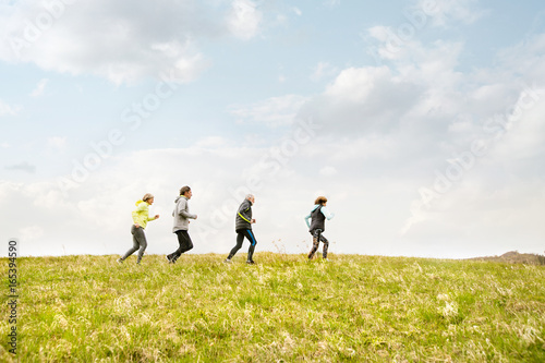 Group of seniors running outside on the green hills.