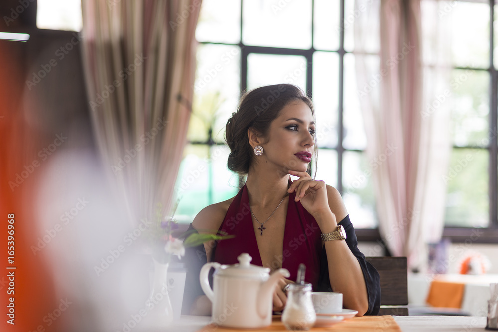 Young business woman grinks coffee at a cafe. Smiling and flirts. Looks at camera Young business woman grinks coffee at a cafe. Smiling and flirts. Looks at camera