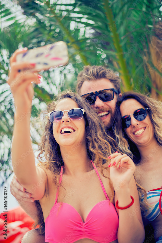 Friends taking selfie at beach, palm tree at background Friends taking selfie at beach, palm tree at background