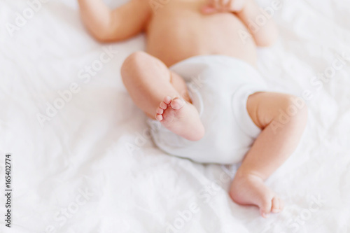 Baby's feet. Little child wearing white bodysuit and diaper. Cozy morning bedtime at home.
