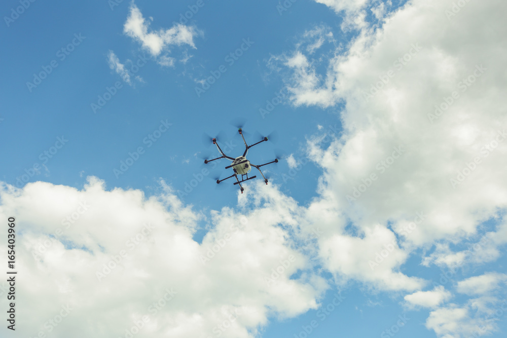 Hovering drone flies in blue sky and taking pictures of green hills. Professional agriculture drone flying in clear blue. Sky partly clouded Hovering drone flies in blue sky and taking pictures of green hills. Professional agriculture drone flying in clear blue. Sky partly clouded
