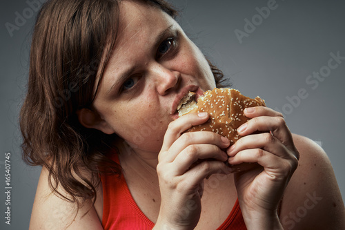 Fat woman on a gray background eating a hamburger, fast food, bad food
