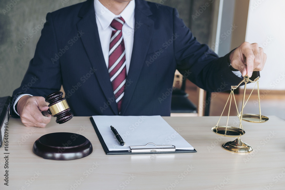 Male lawyer working with gavel and scales of justice, note paper, report the case on wooden table in office, Law and justice concept Male lawyer working with gavel and scales of justice, note paper, report the case on wooden table in office, Law and justice concept