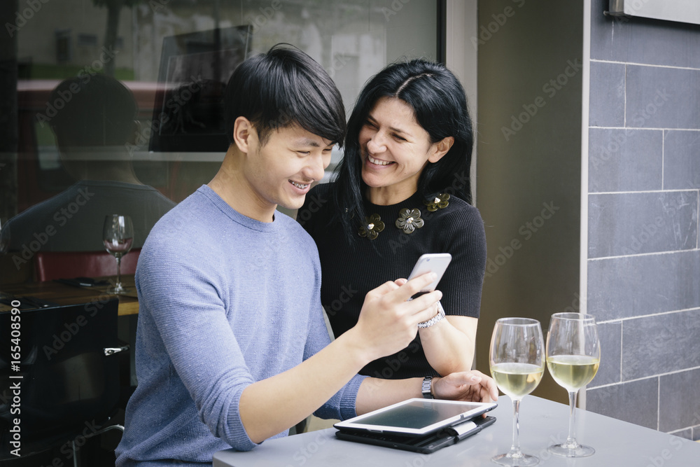 Multiethnic couple in a restaurant looking at phone with a glass of white wine