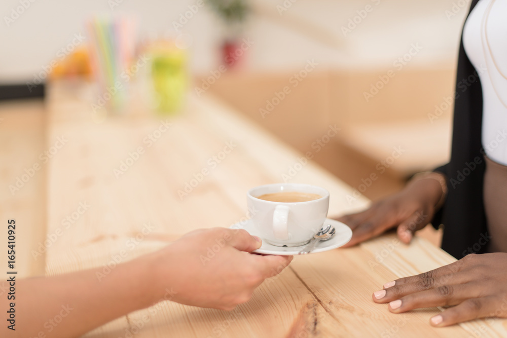 cropped view of waiter giving cup of coffee to african american woman in cafe cropped view of waiter giving cup of coffee to african american woman in cafe