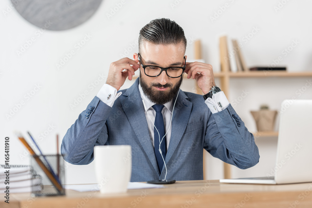 portrait of businessman putting earphones into ears at workplace in office
